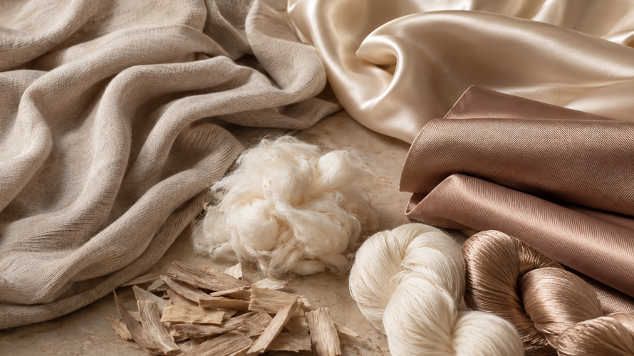 Modal and silk fabric swatches with fibre labels, smooth drape, yarn cones and a comparison card on a neutral table